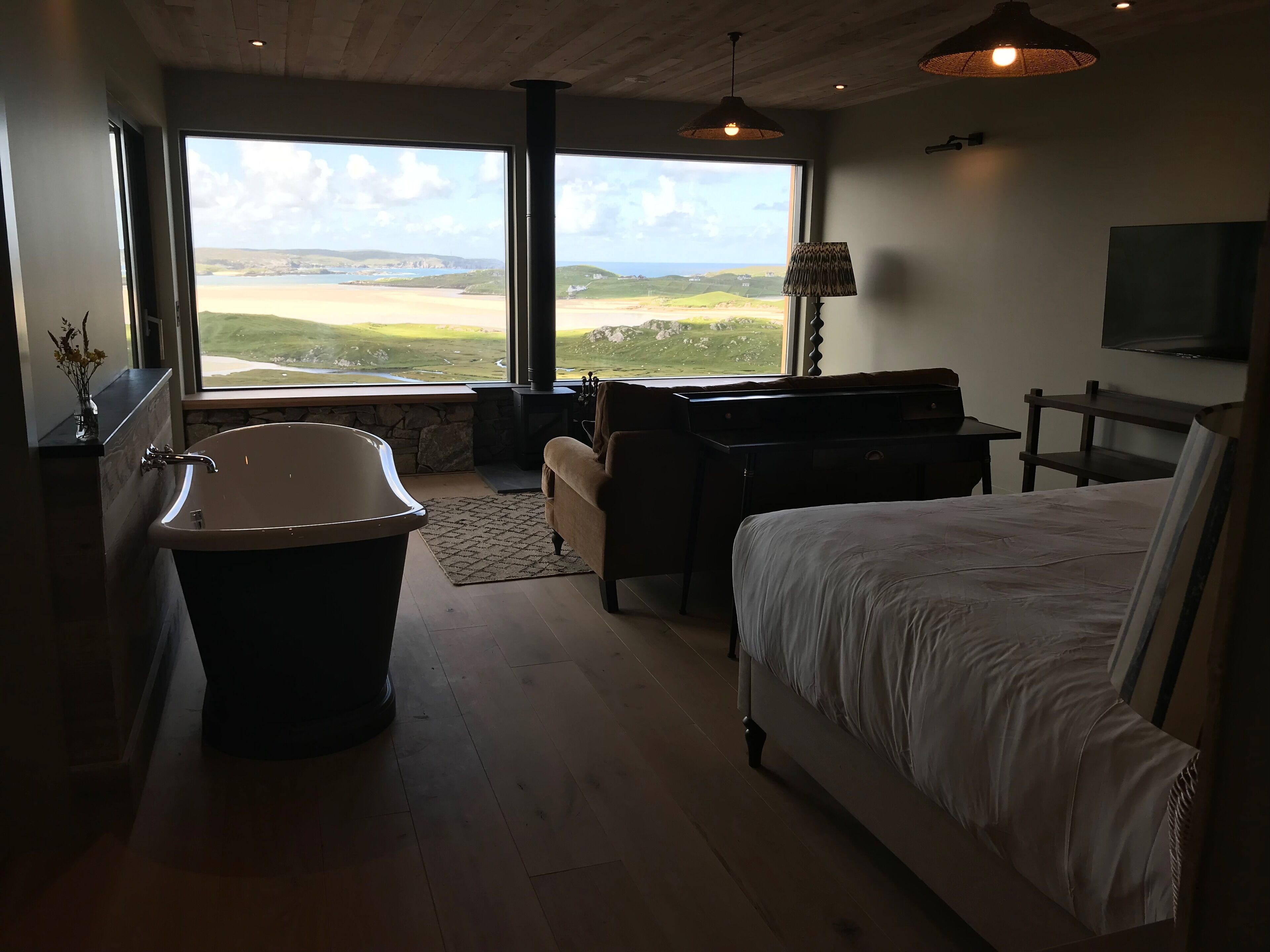 Una camera da letto con un letto grande, una vasca, una scrivania e vista sulla costa.