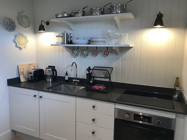 A modern kitchen with white cabinets, a black countertop, a built-in oven, and a hanging pot rack. - Uig Sands Rooms (Isle of Lewis)