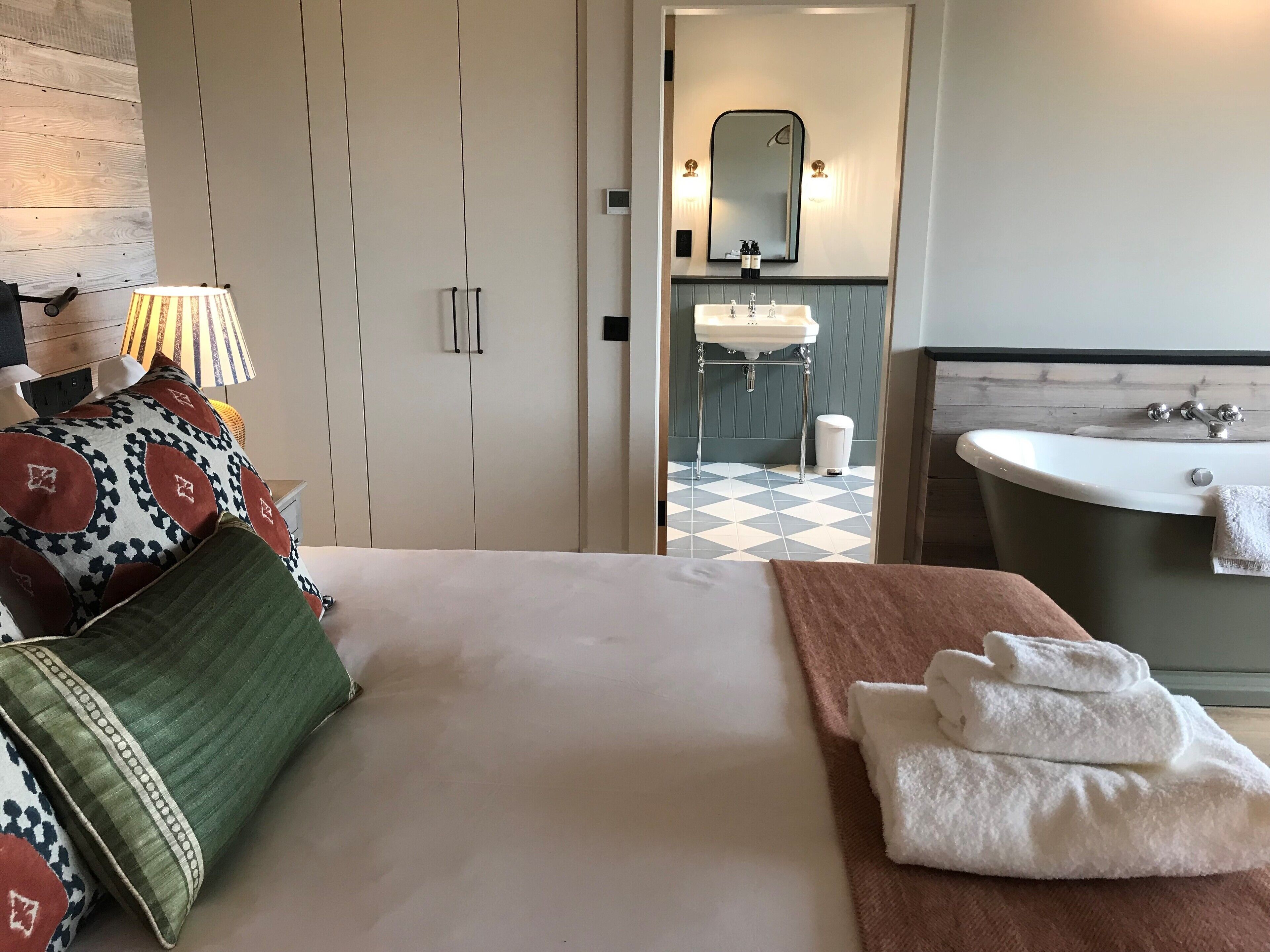 Una camera d'hotel con un letto, un bagno con lavandino e vasca, e uno specchio.