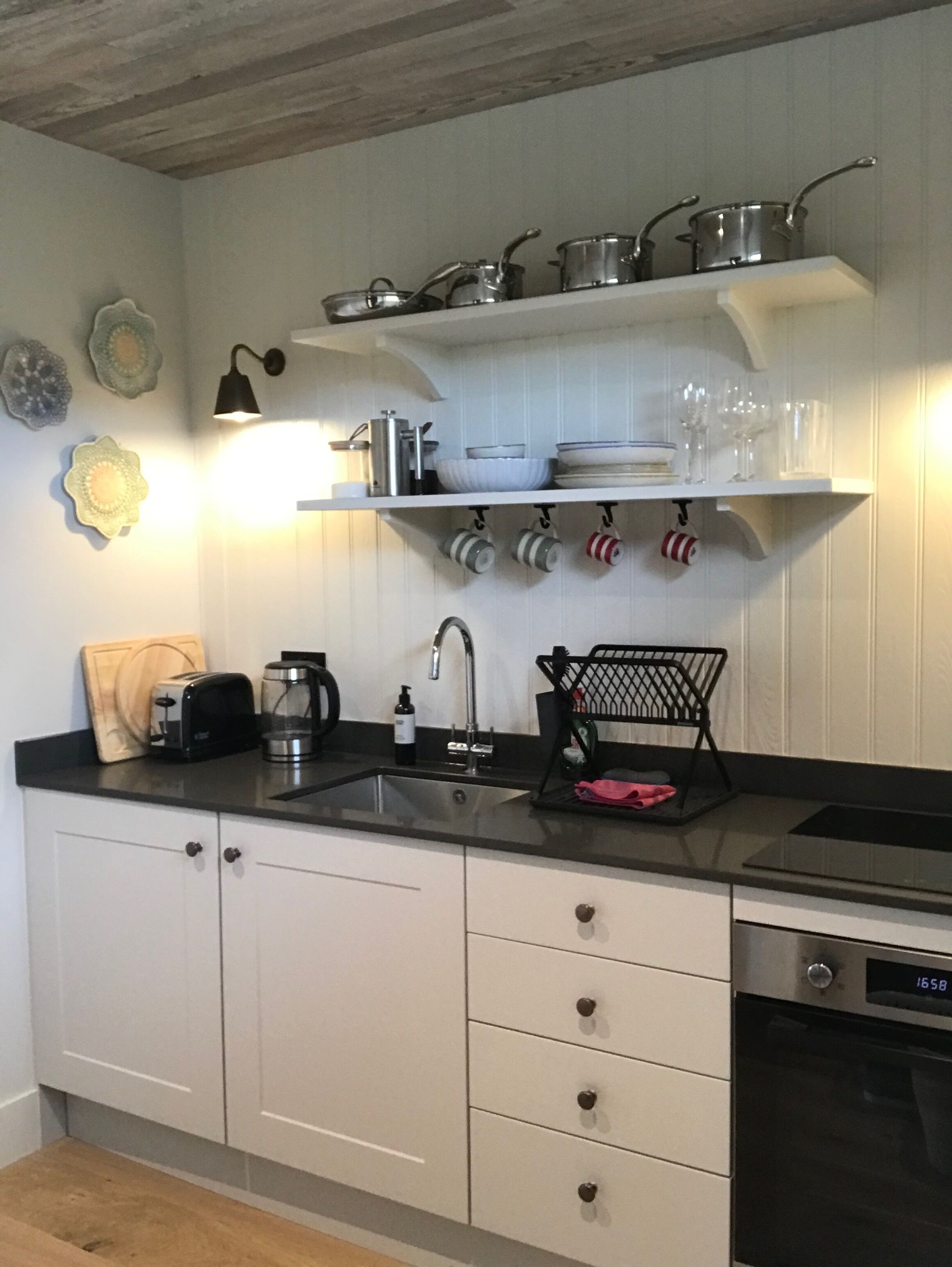 A kitchen with white cabinets, a black countertop, and a built-in oven. There are shelves above the sink holding dishes and glasses.
