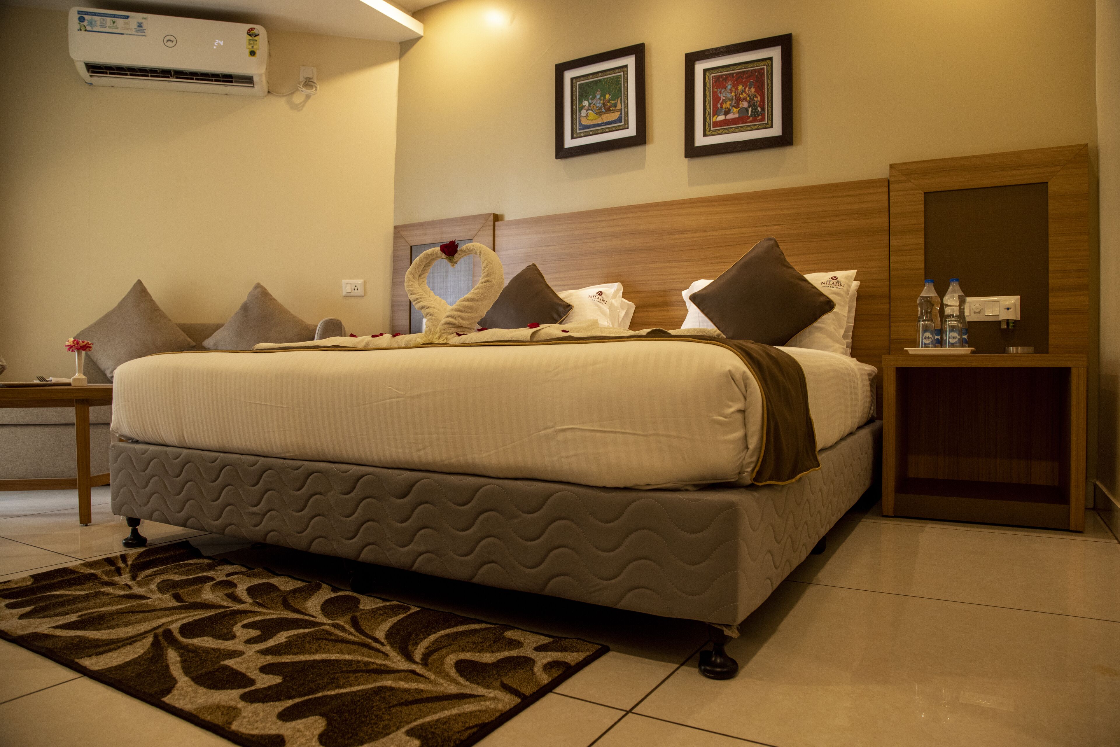 Un cuarto de hotel con una cama grande, una mesita de noche, aire acondicionado instalado en la pared y dos cuadros enmarcados.