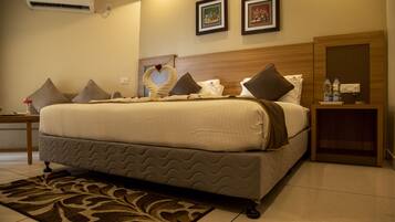 Un cuarto de hotel con una cama grande, una mesita de noche, aire acondicionado instalado en la pared y dos cuadros enmarcados.