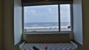 A room with a large window overlooking the ocean, a cushioned bench, and a small plant.
