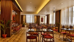 A spacious dining area with multiple tables and chairs, a patterned floor, and large windows with curtains.