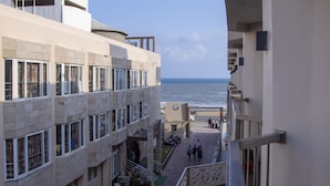 A hotel corridor with a view of the sea, featuring a central walkway, balconies, and a clock tower.