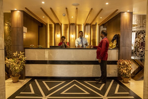 A hotel reception area with a modern design, featuring a reception desk, a large potted plant, and a geometric patterned floor.