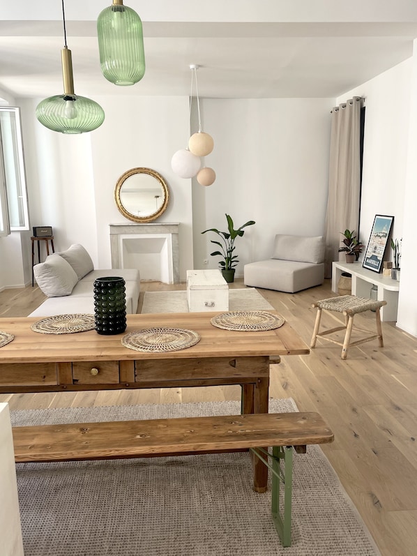 Una sala de estar moderna con una mesa de comedor de madera, un banco, un sofá blanco, una mesita auxiliar blanca y una lámpara colgante verde.