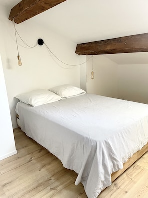Un dormitorio con cama, vigas de madera y dos lámparas colgantes.