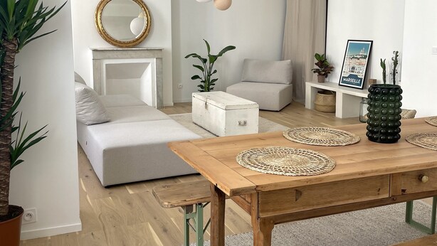 A modern living room with a wooden dining table, white sofas, and a large mirror.