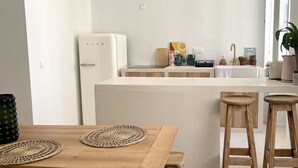 A modern kitchen with a central island, wooden stools, and pendant lighting.