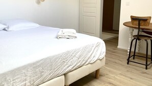A bedroom with a bed, a hanging light, a wooden chair, and a door leading to another room.