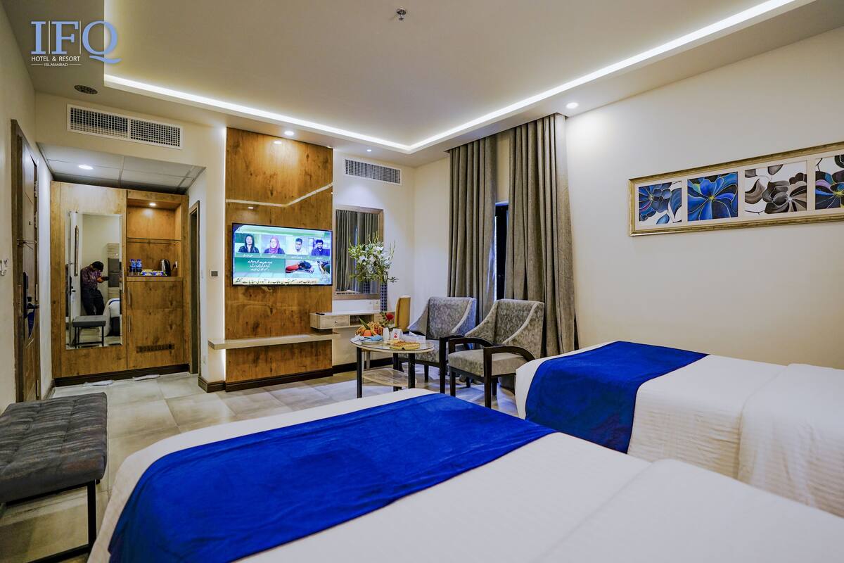 Ein Hotelzimmer mit zwei Betten, einem Fernseher, einem Schreibtisch und einem Stuhl.