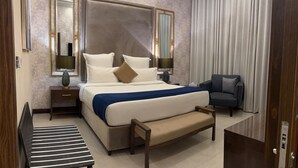 Ein modernes Hotelzimmer mit einem großen Bett, Nachttischen, einer Bank, einem Sessel und einem großen Fenster mit Vorhängen.