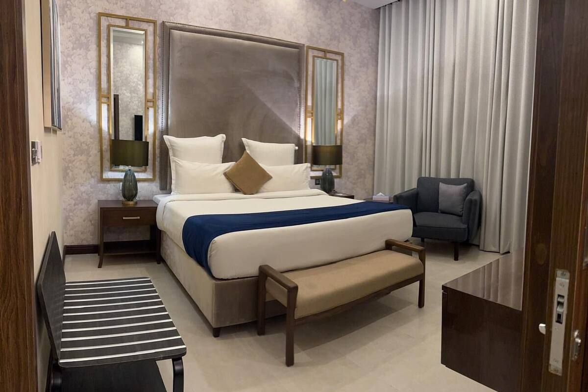 Ein modernes Hotelzimmer mit einem großen Bett, Nachttischen, einer Bank, einem Sessel und einem großen Fenster mit Vorhängen.