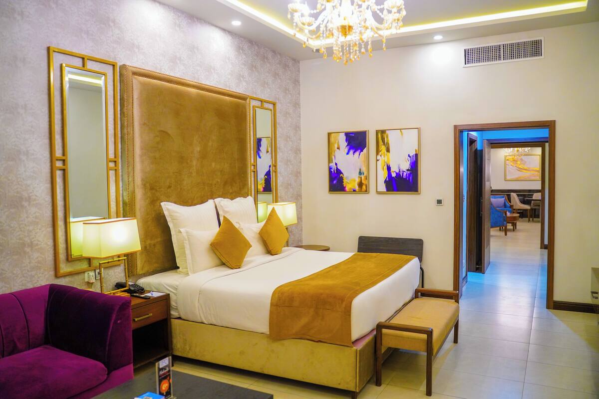 Ein Hotelzimmer mit einem großen Bett, einem violetten Sessel, einem Schreibtisch und einer Chandelüster.
