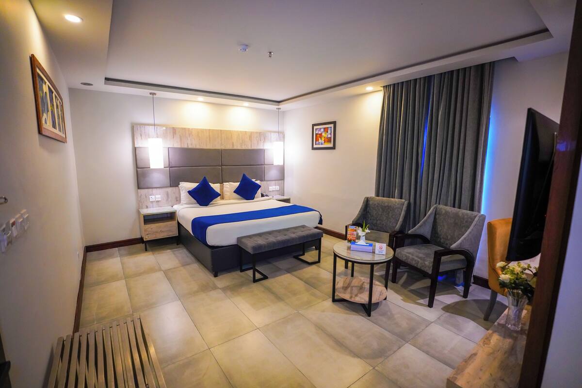 Ein Hotelzimmer mit einem großen Bett, zwei Sesseln, einem kleinen Tisch und einem Fernseher.