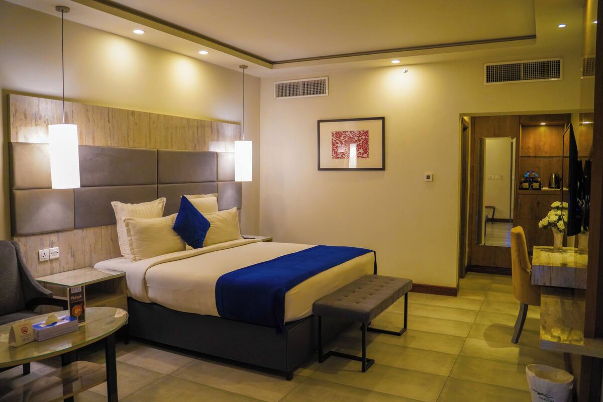 Ein Hotelzimmer mit Bett, Nachttisch, Bank und einem kleinen Tisch mit Taschentuchbox.