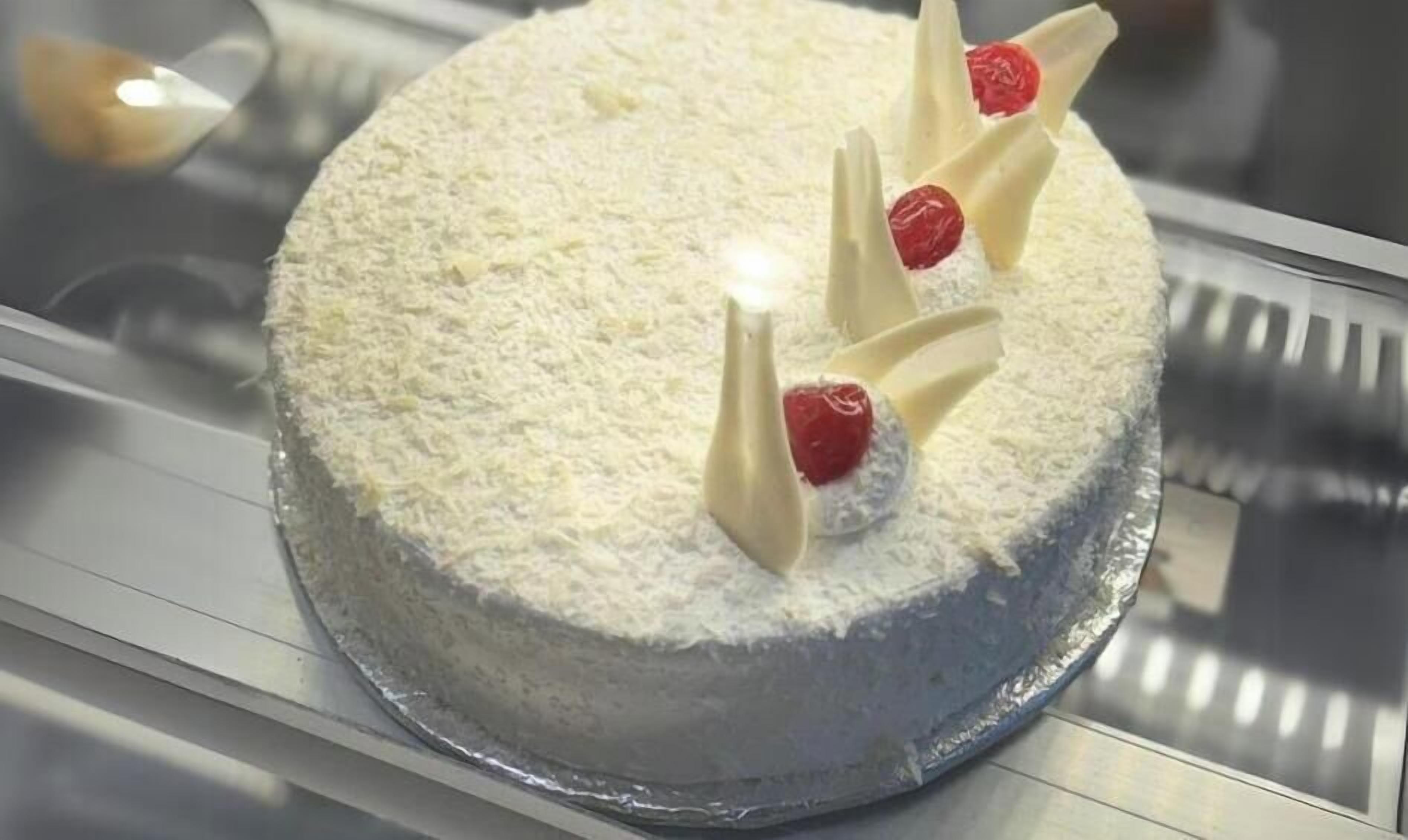 A creamy cake with decorative chocolate pieces and strawberries on a display counter.