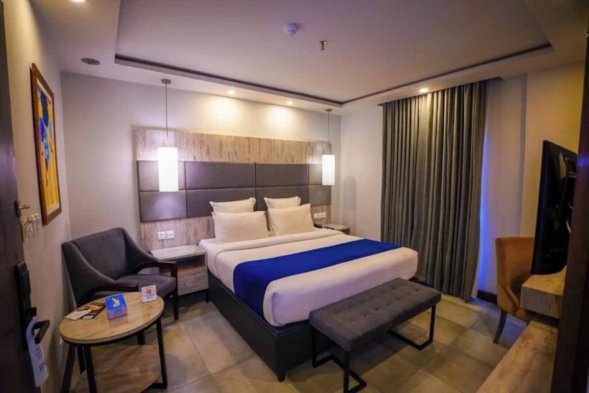 Ein Hotelzimmer mit Bett, Nachttischen, Schreibtisch, Stuhl, Bank und einem großen Fenster mit Vorhängen.