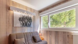 A modern living room with a wooden wall, a large window, and a sofa with cushions. - Les Lauzes D25 by Interhome (Les Menuires)