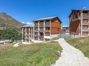 A modern hotel with multiple floors, balconies, and a dirt path leading to the entrance.