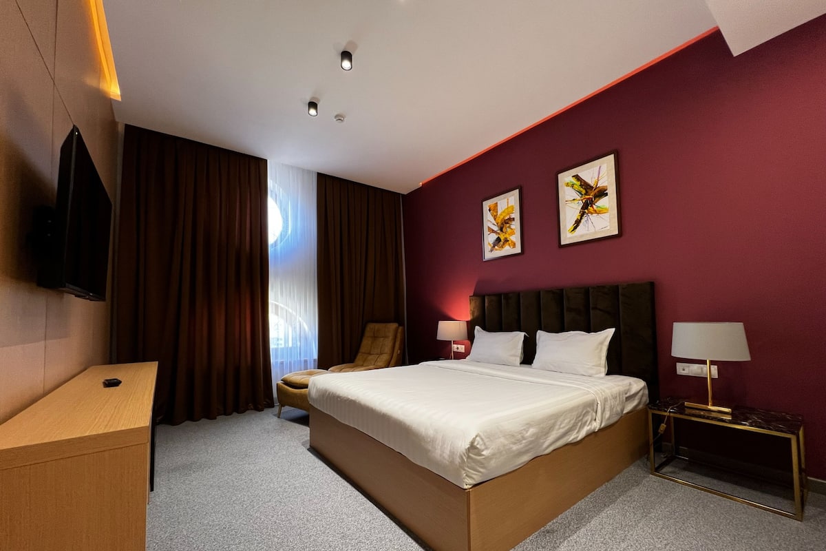 A hotel room with a large bed, a desk, a chair, two wall-mounted lamps, and artwork on the wall.