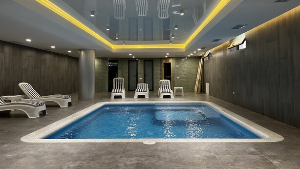 A modern indoor swimming pool with a clear blue water, surrounded by lounge chairs and a high ceiling with recessed lighting.