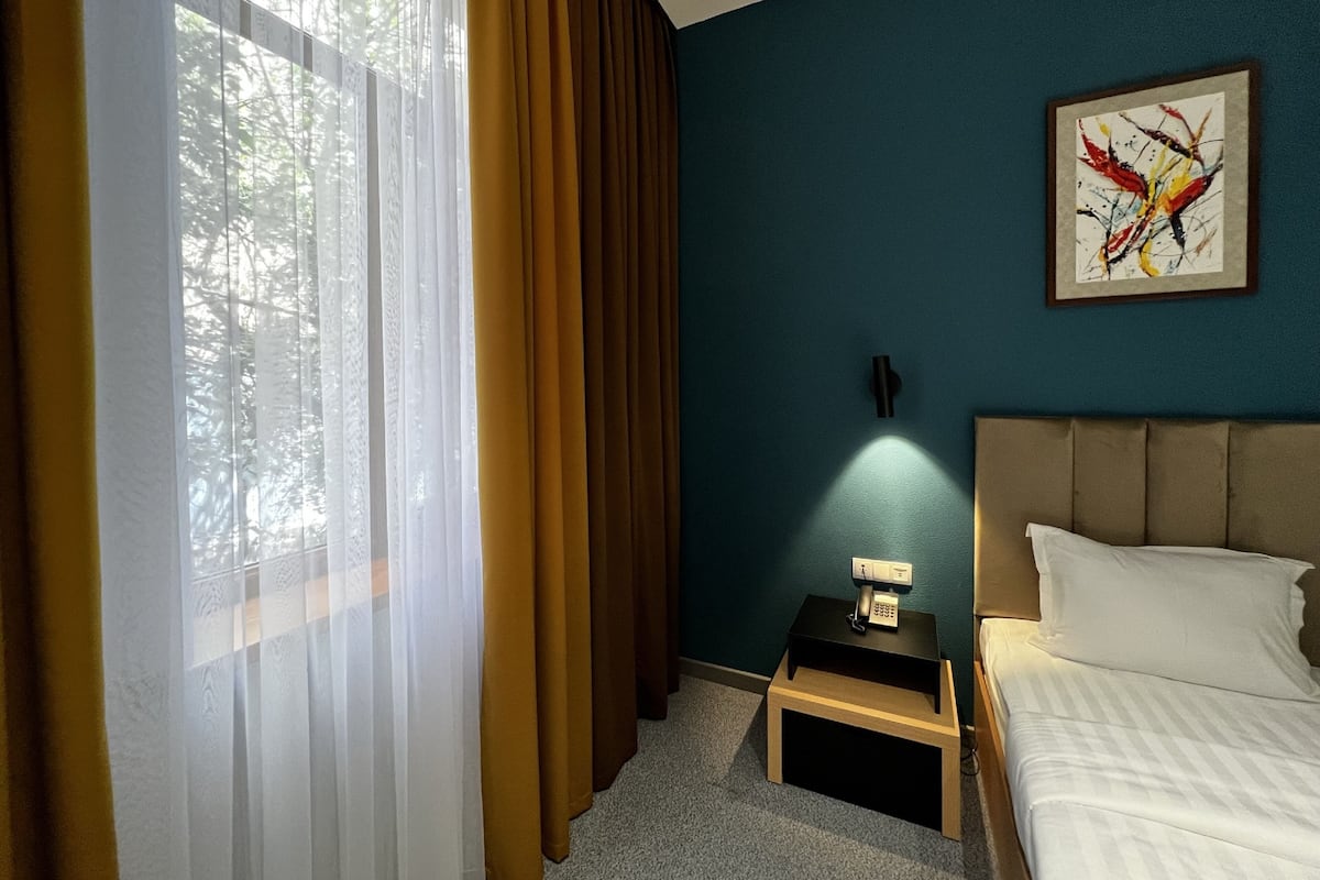 A hotel room with a bed, a nightstand with a phone, a wall-mounted light, and a painting.