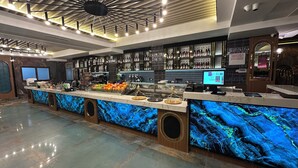 A modern bar area with a marble countertop, a variety of bottles, and a digital screen.