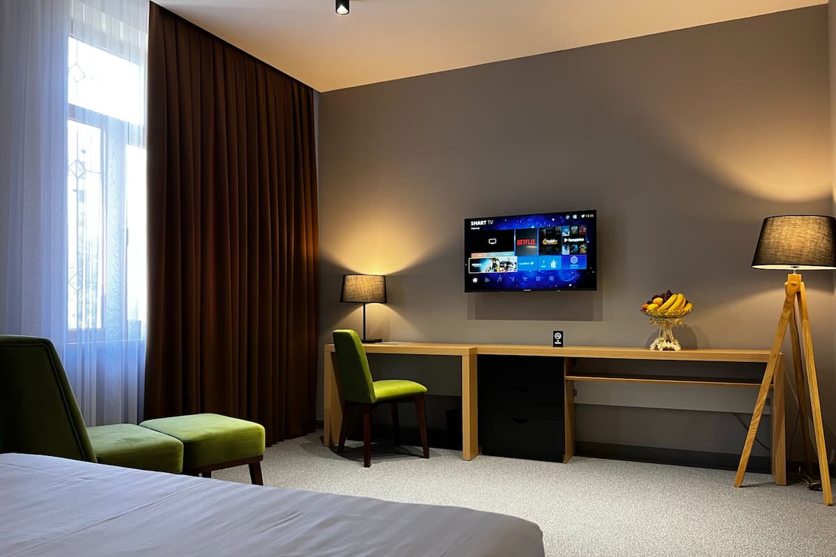 A hotel room with a bed, a desk, a chair, a TV mounted on the wall, and a lamp.
