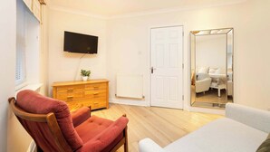 A bedroom with a wooden dresser, a television mounted on the wall, a white door, and a large mirror.