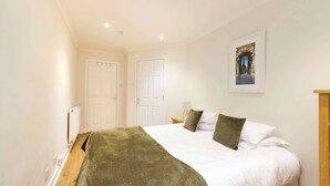 A bedroom with a bed, white walls, a framed picture, and a radiator. - Gorgeous Apartment near Edinburgh Castle (Edinburgh)