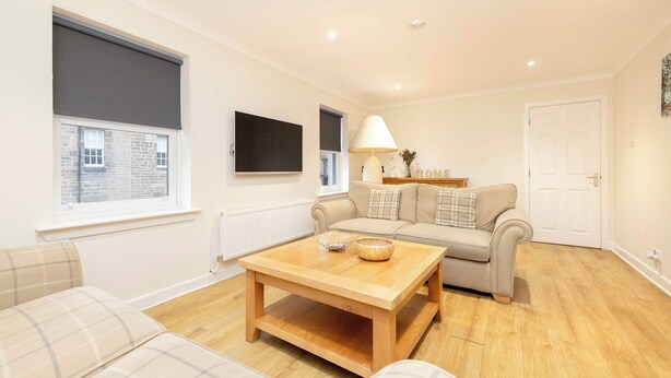 A living room with a sofa set, a coffee table, a lamp, and a TV on the wall. - Gorgeous Apartment near Edinburgh Castle (Edinburgh)