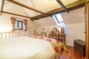 Quarto com cama, penteadeira, espelho e claraboia.