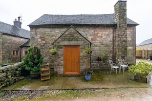 A stone cottage with a wooden door, a small garden with potted plants, and a stone wall.