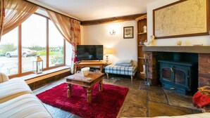 Ein gemütliches Wohnzimmer mit Kamin, Fernseher und einem großen Fenster mit Vorhängen.