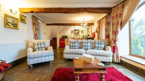 Ein gemütliches Wohnzimmer mit zwei Sofas, einem roten Teppich und einem Holztisch. Im Hintergrund ist eine Küche zu sehen.