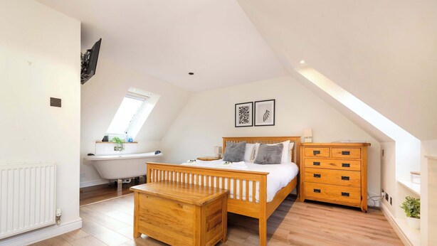 A bedroom with a sloped ceiling, a wooden bed, a wooden dresser, a wooden nightstand, a white radiator, a window, and a skylight. - Modern Apartment close to Dean Village (Edinburgh)
