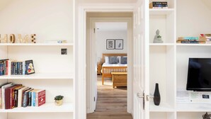 A hallway leading to a bedroom with a wooden bed, a TV on the wall, and bookshelves on either side. - Modern Apartment close to Dean Village (Edinburgh)