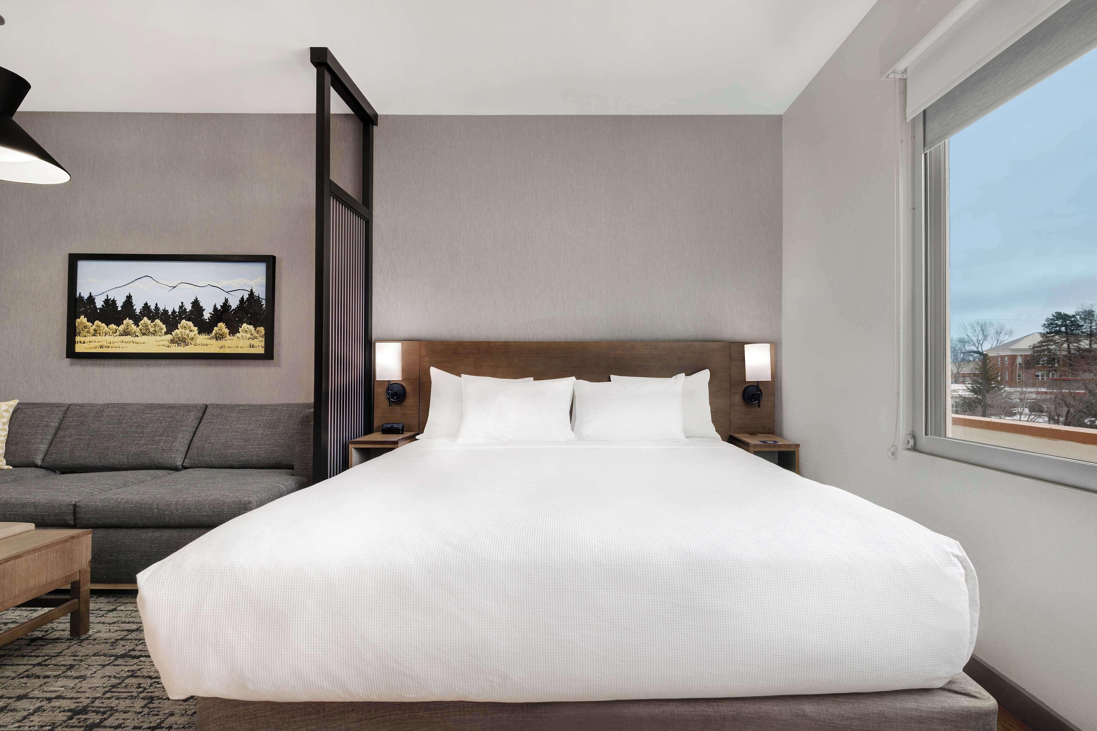 Una habitación de hotel con una cama grande, un sofá, una mesita de noche y una lámpara de pared.