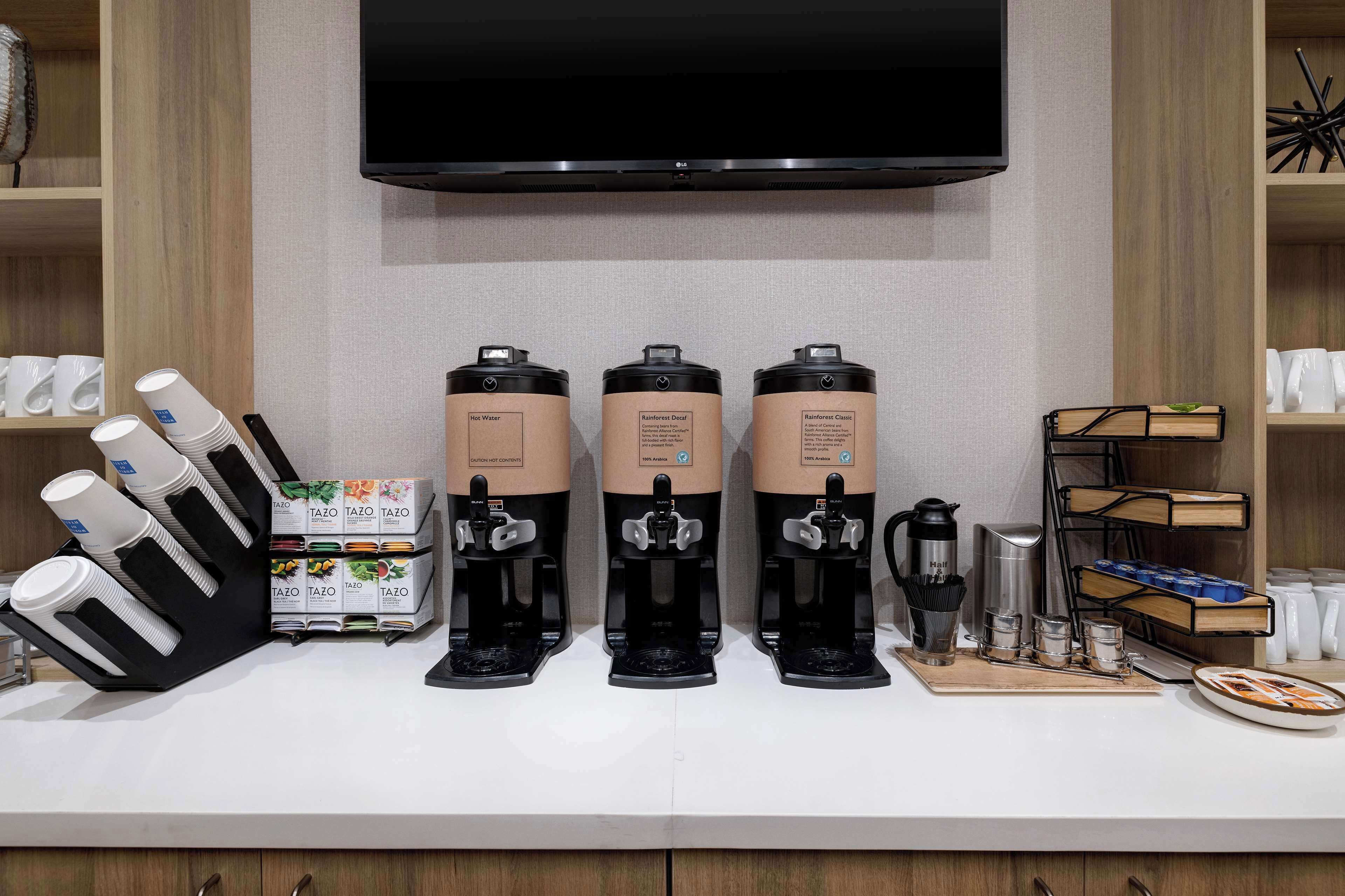 A coffee station with three coffee dispensers, a coffee maker, and a tray with cups and utensils.