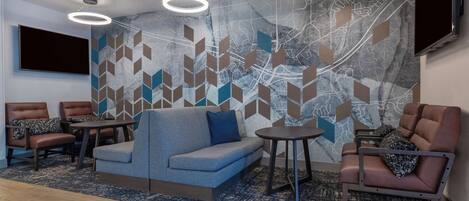 A modern lounge area with a sofa, armchairs, and tables, featuring a geometric patterned wall and a flat-screen TV.