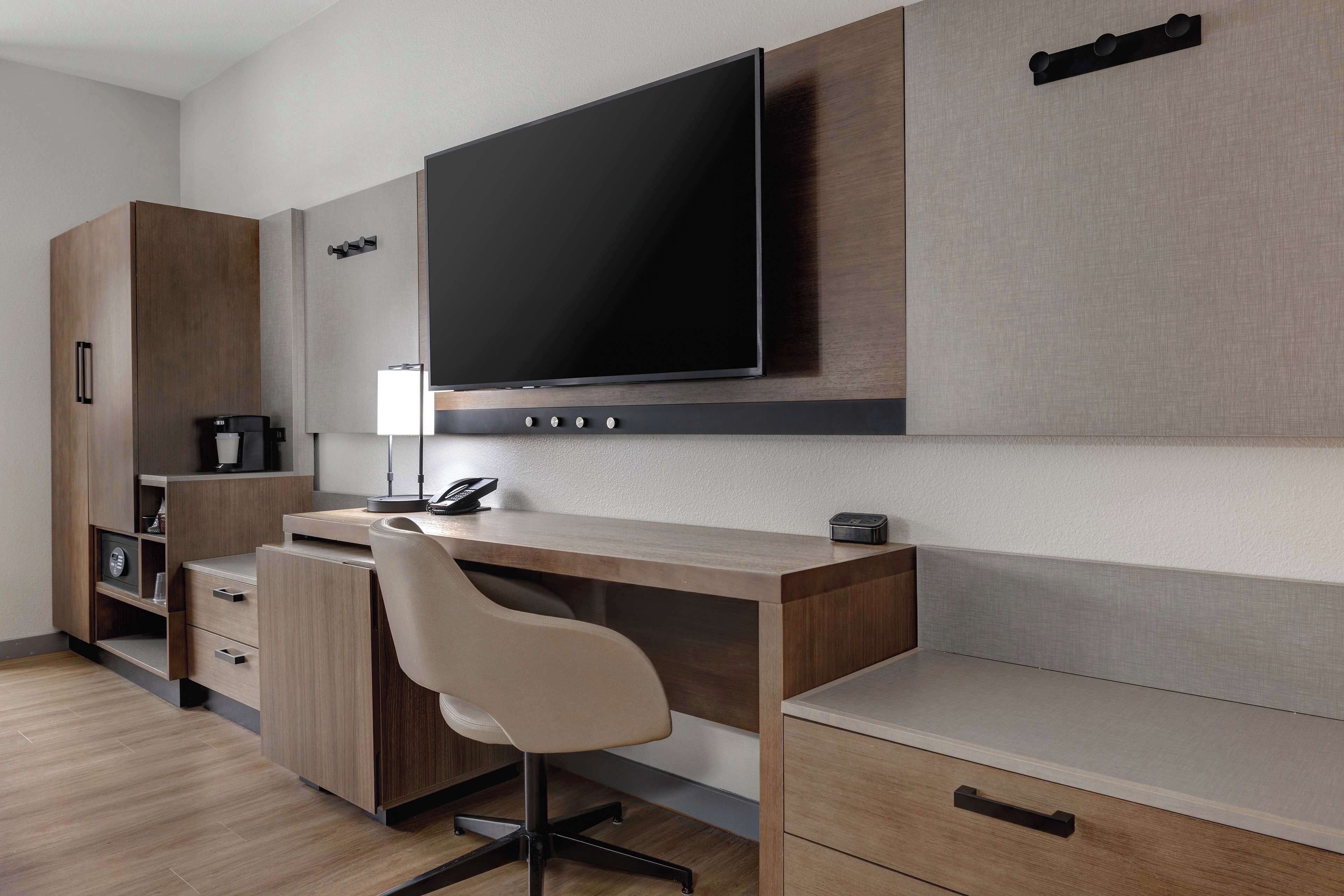 Una cocina moderna con televisión integrada, armarios de madera, encimera de color claro y una silla.