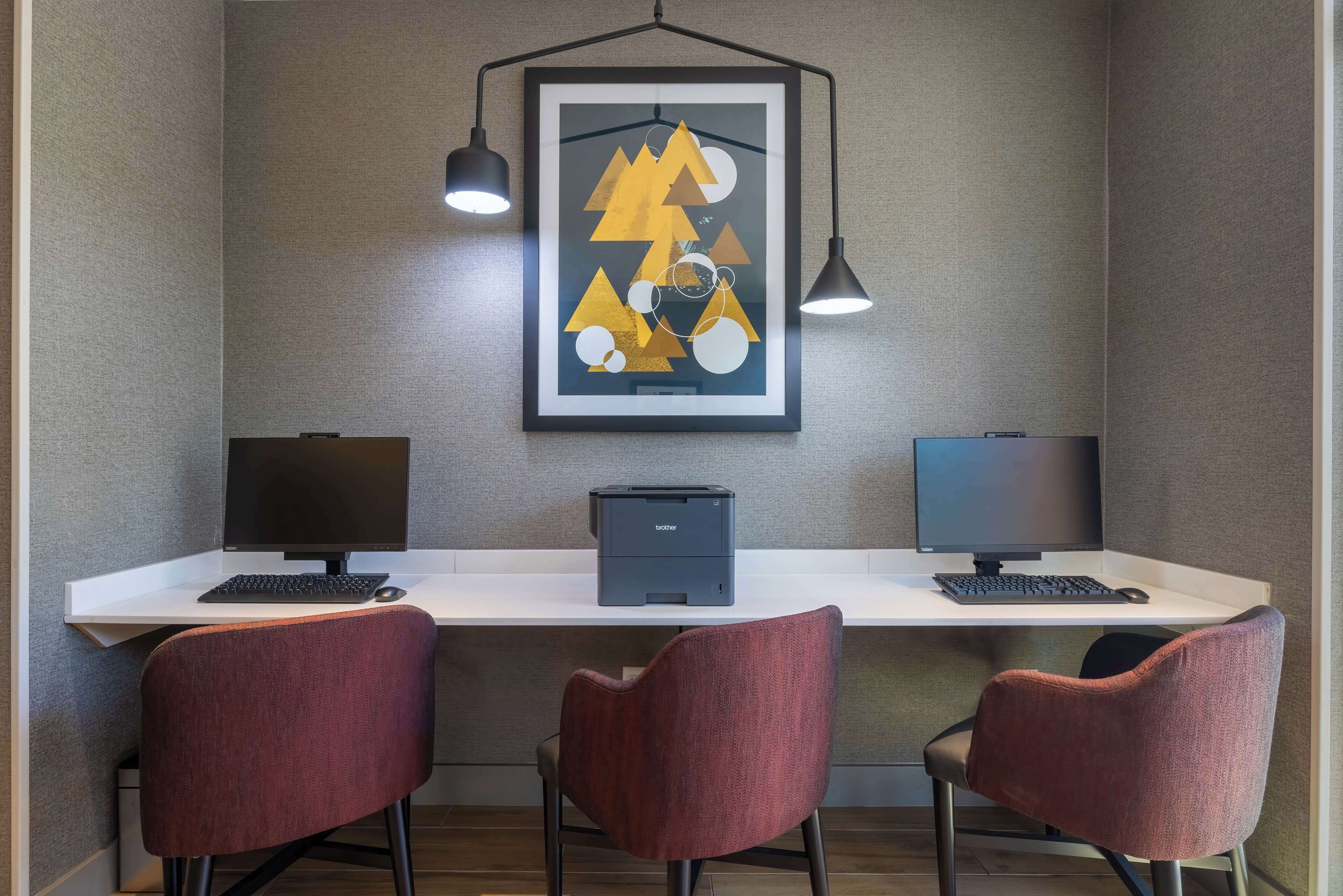 A workspace with two monitors, a printer, and two chairs.