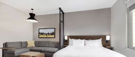 Et moderne hotelværelse med en stor seng, en grå sofa, et lille sofabord og et billede på væggen.