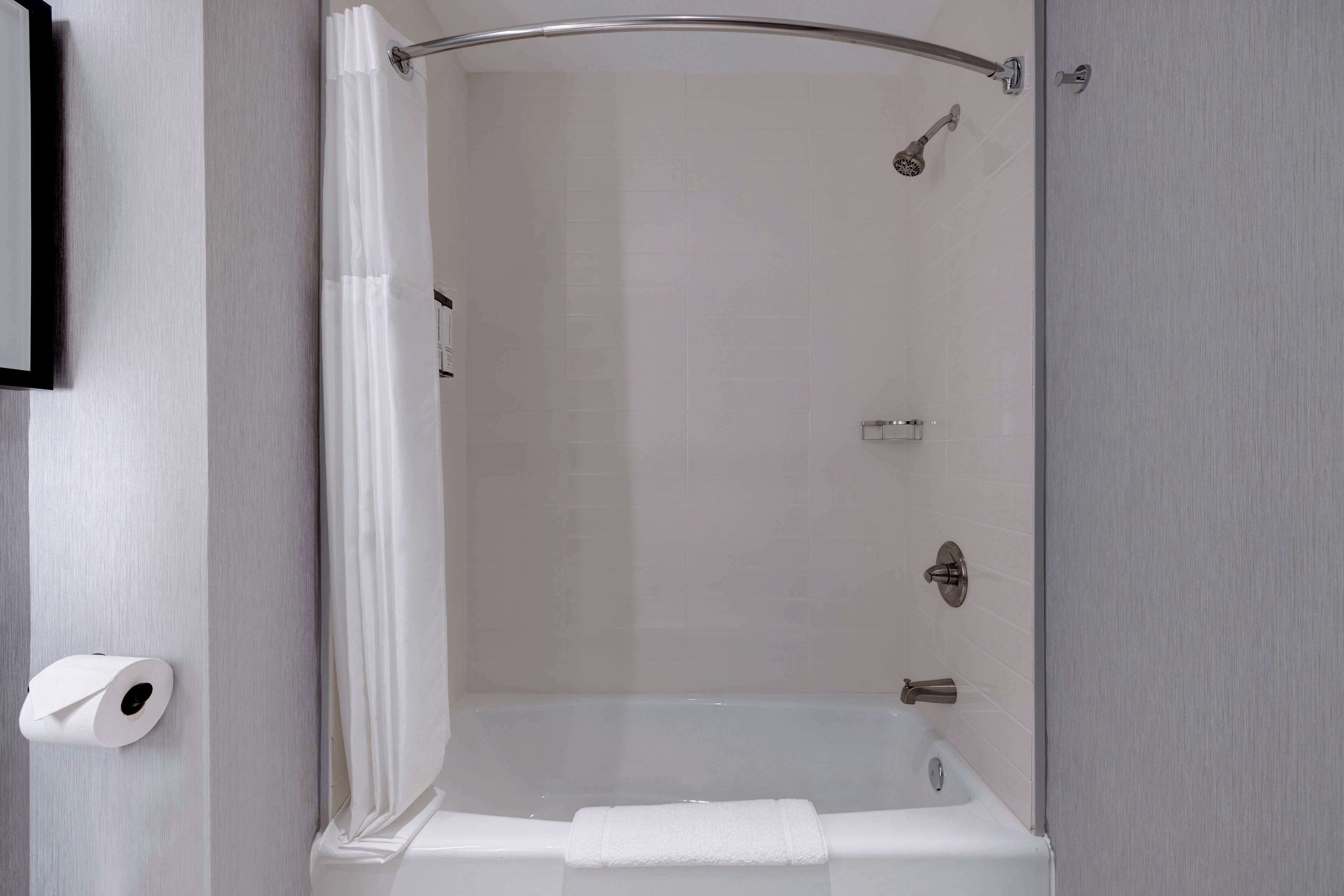 A modern bathroom with a glass-enclosed shower, a white bathtub, and a toilet paper holder on the wall.
