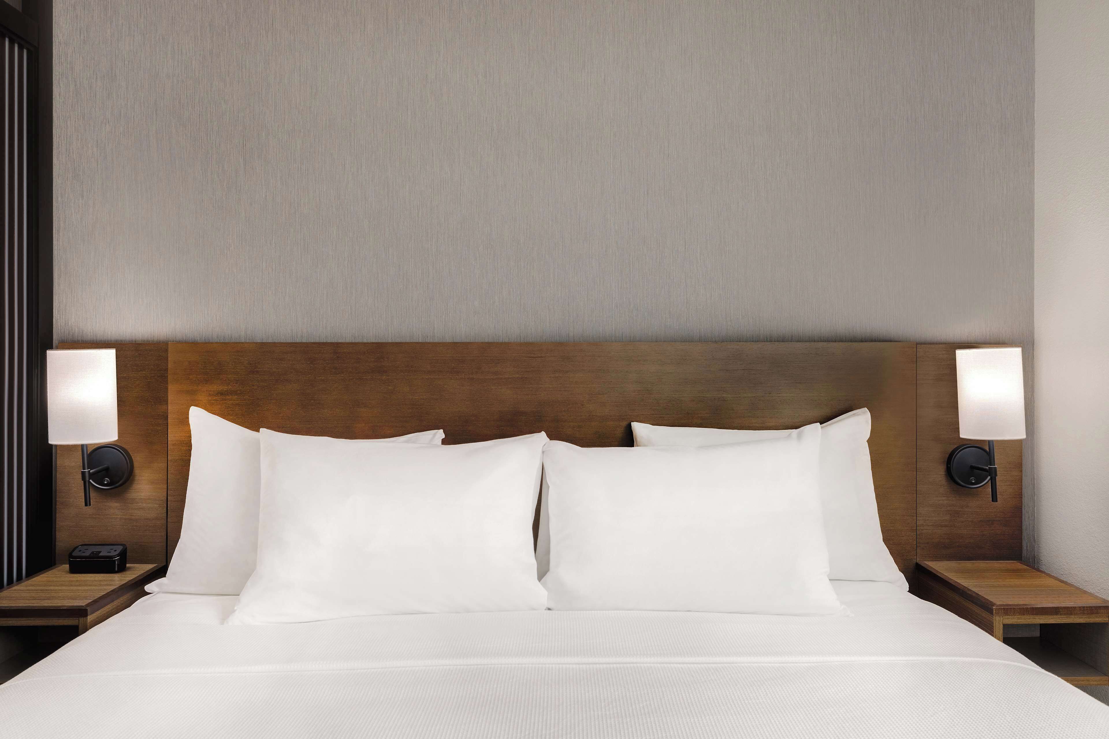 A neatly made bed with white linens, two bedside lamps, and a wooden headboard.