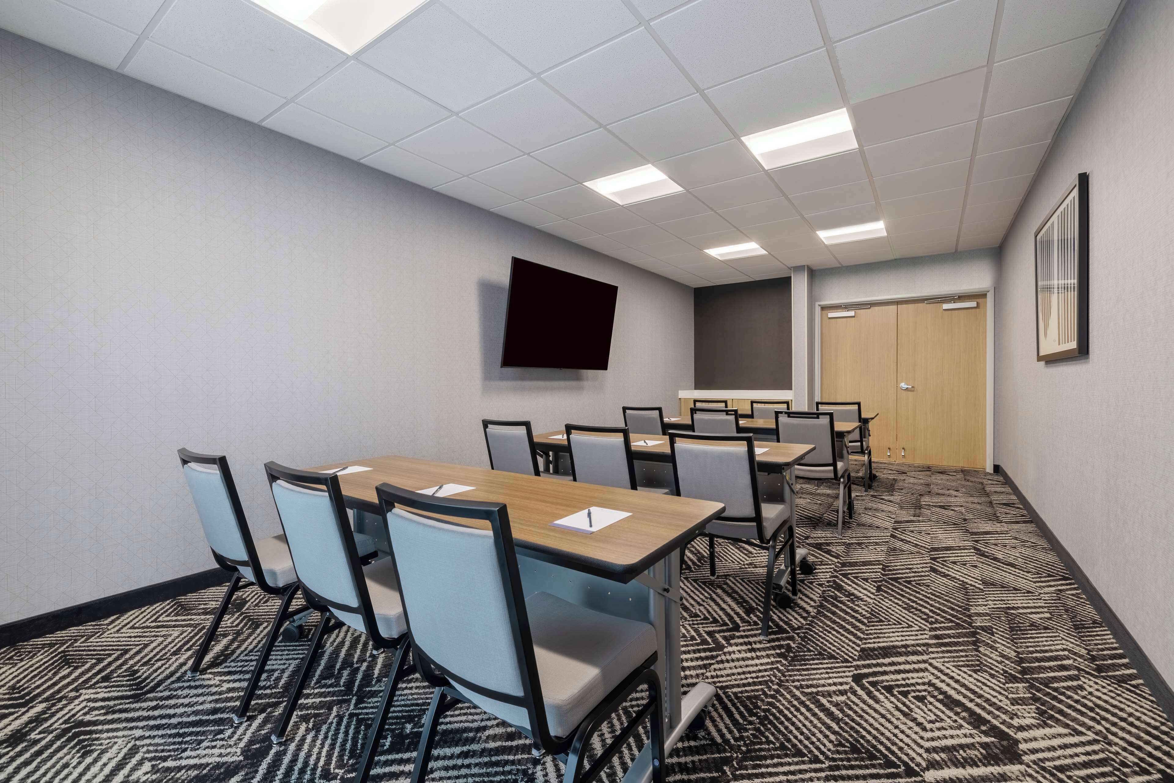 A conference room with a large table, chairs, a flat-screen TV, and a carpeted floor.