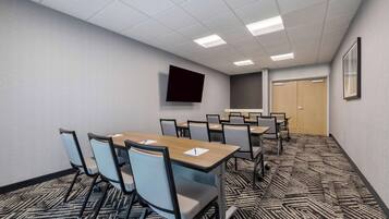 A conference room with a large table, chairs, a flat-screen TV, and a carpeted floor.