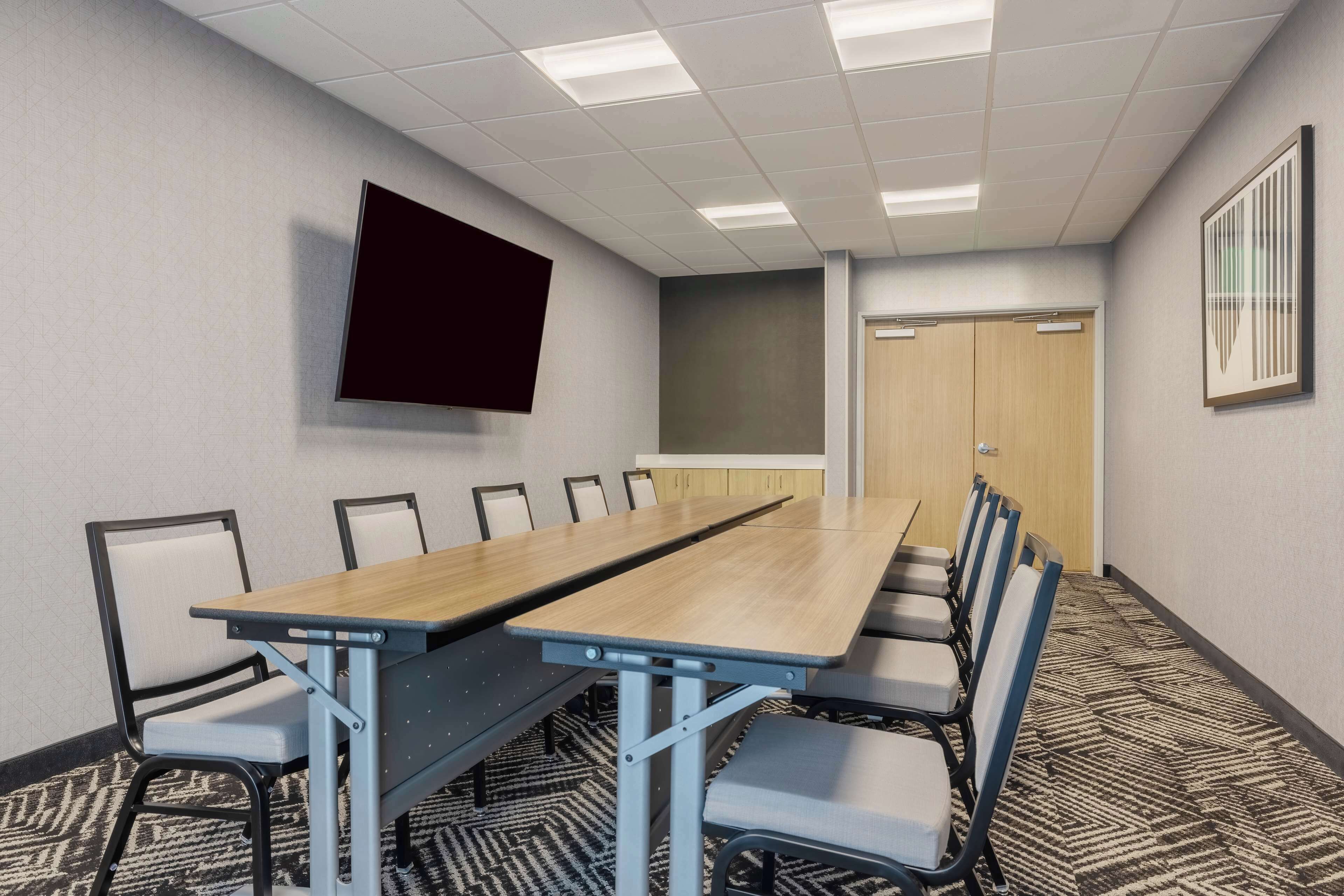 A conference room with a long table, chairs, a projector screen, and a door.